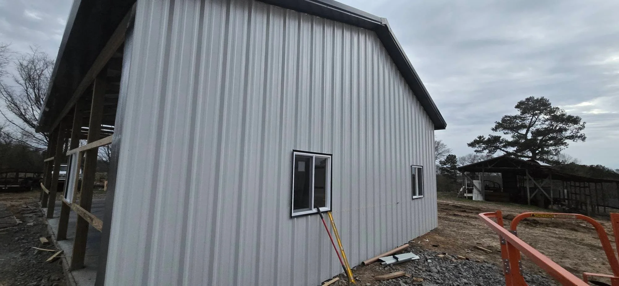 Metal building with corrugated steel siding, black-trimmed windows, and covered porch on cleared property