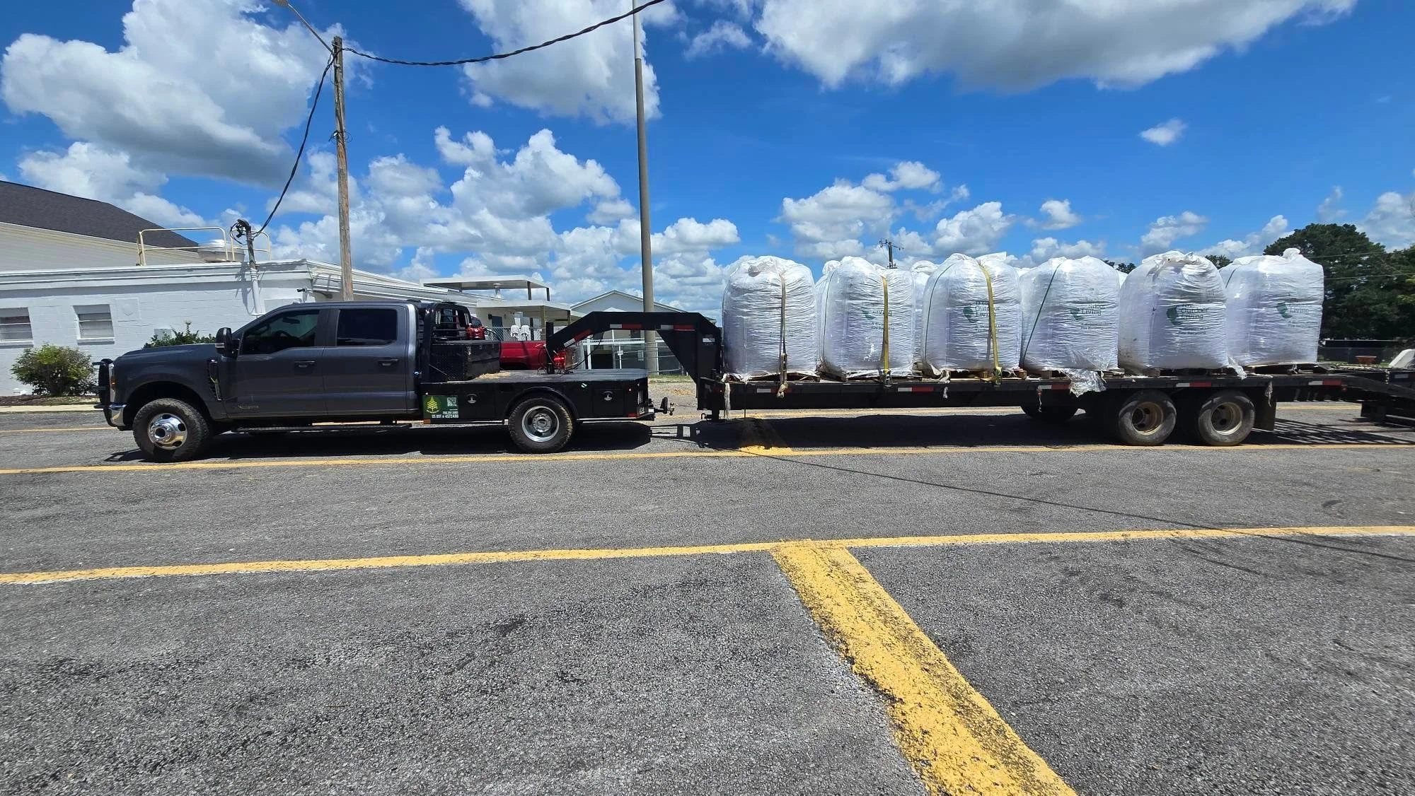 Flatbed trailer loaded with six wrapped bulk material bundles, commercial hauling truck