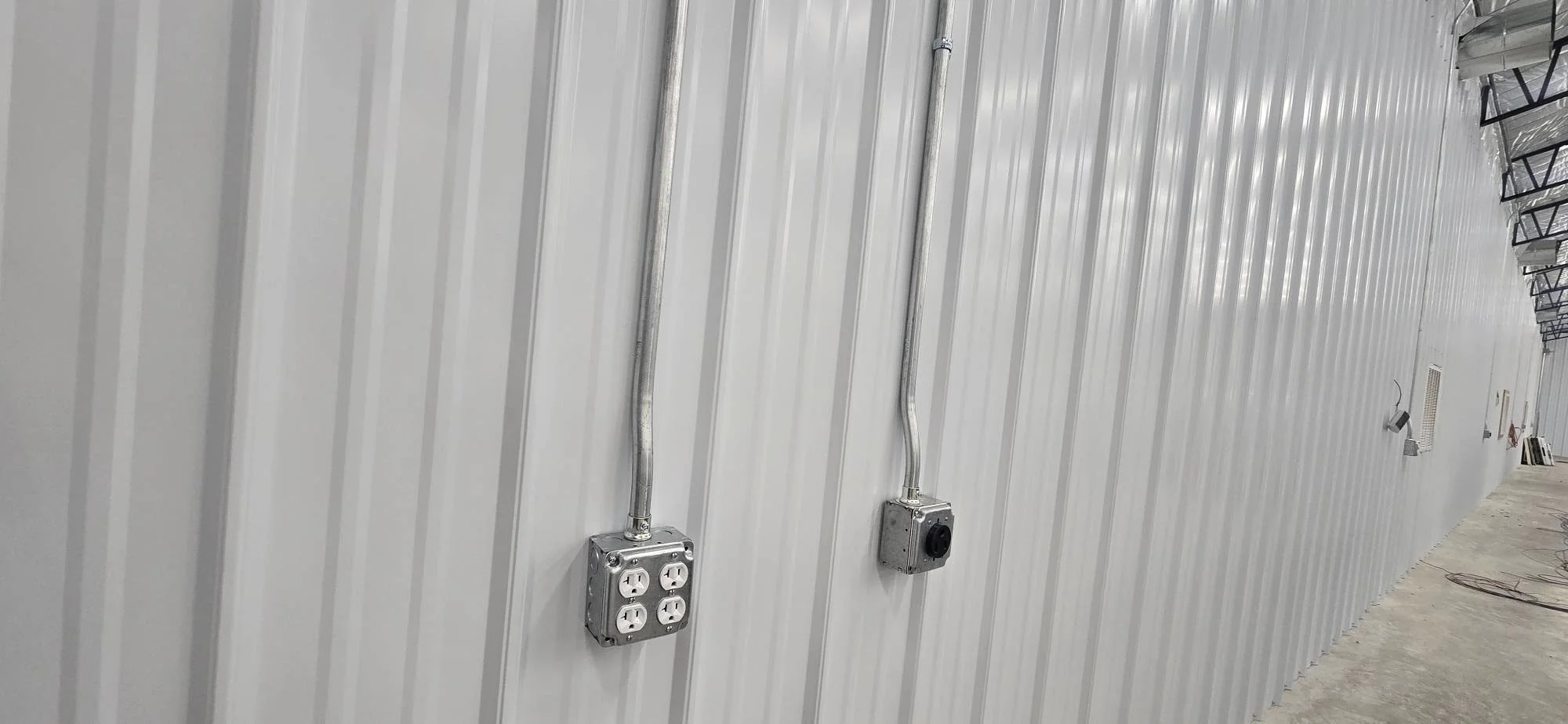 Metal building interior with electrical conduit and outlet boxes installed on corrugated walls