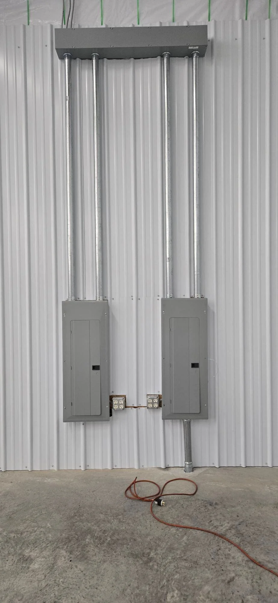 Two gray electrical panels with vertical steel conduit runs on metal building wall