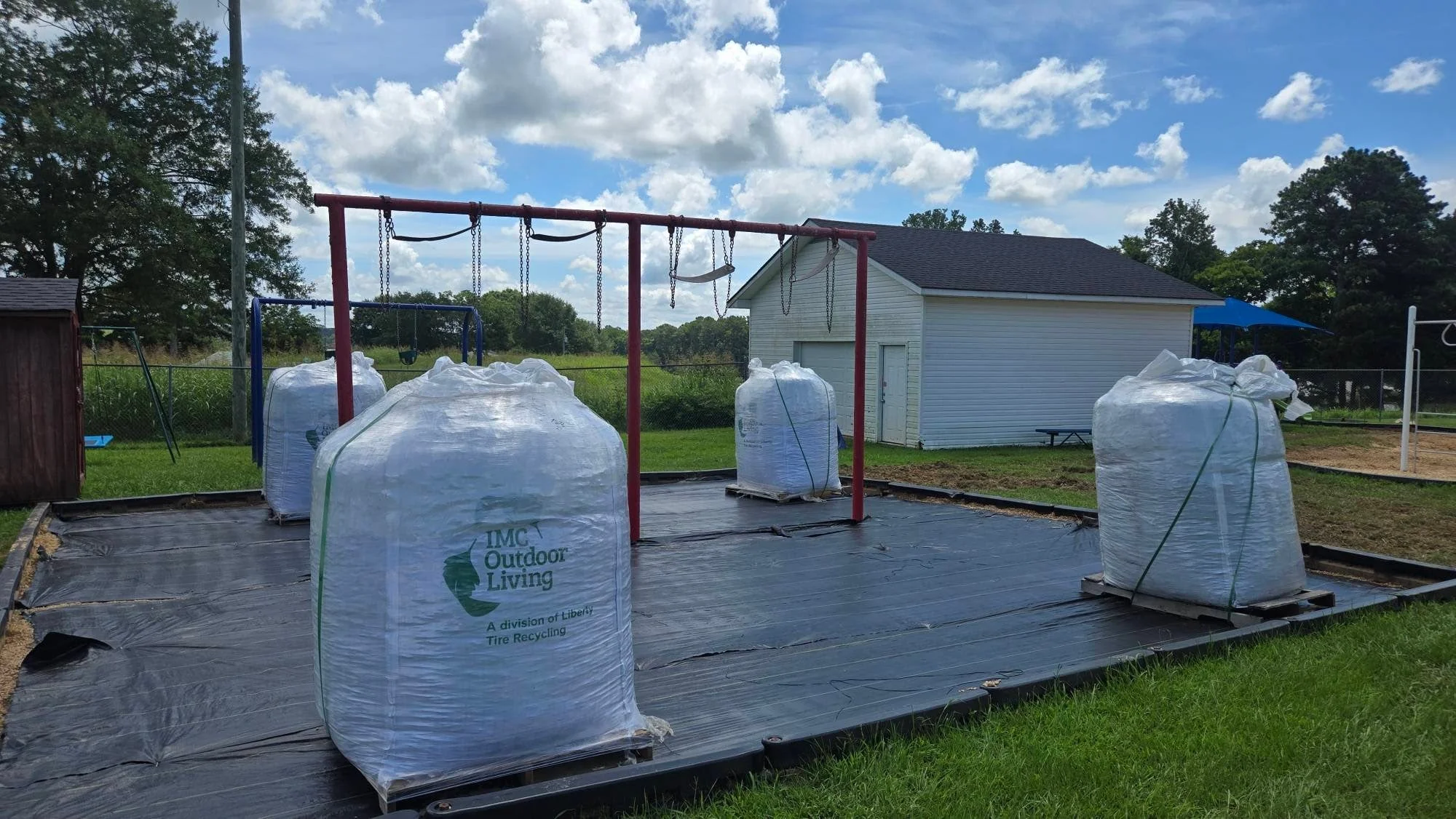 Black landscape fabric covering cleared lot with stacked mulch bags and metal swing set frame