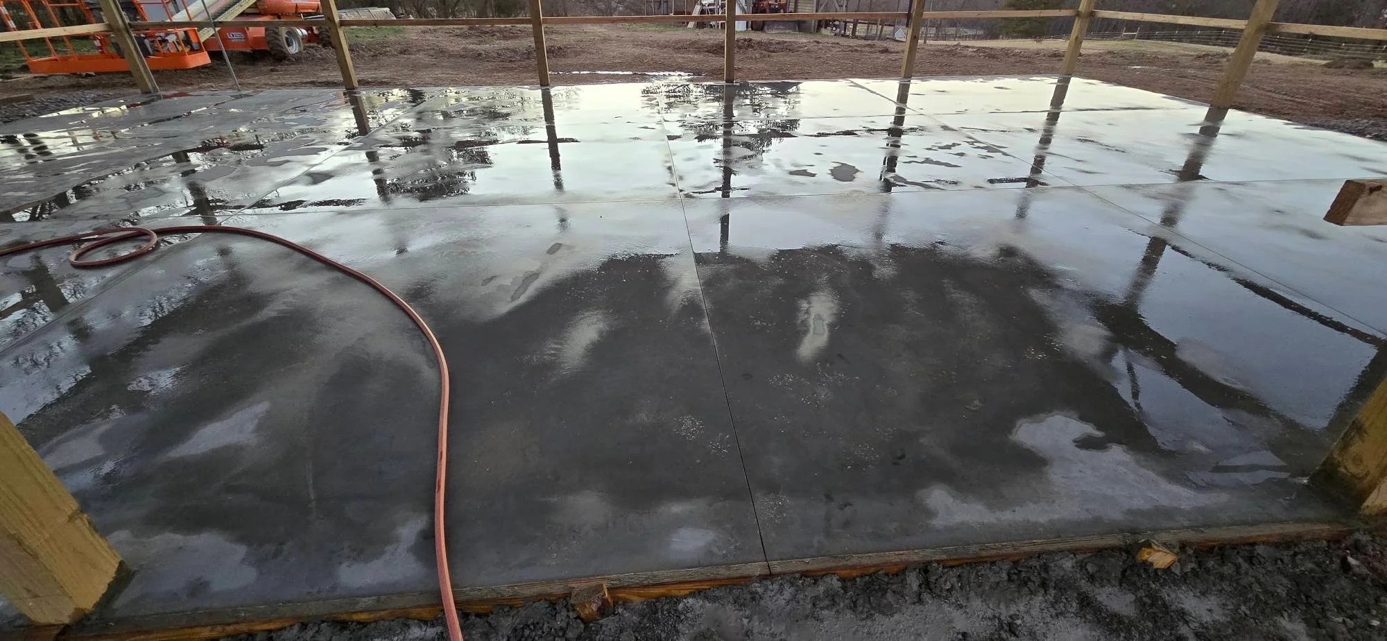 Freshly poured concrete foundation pad with drainage and wooden support posts