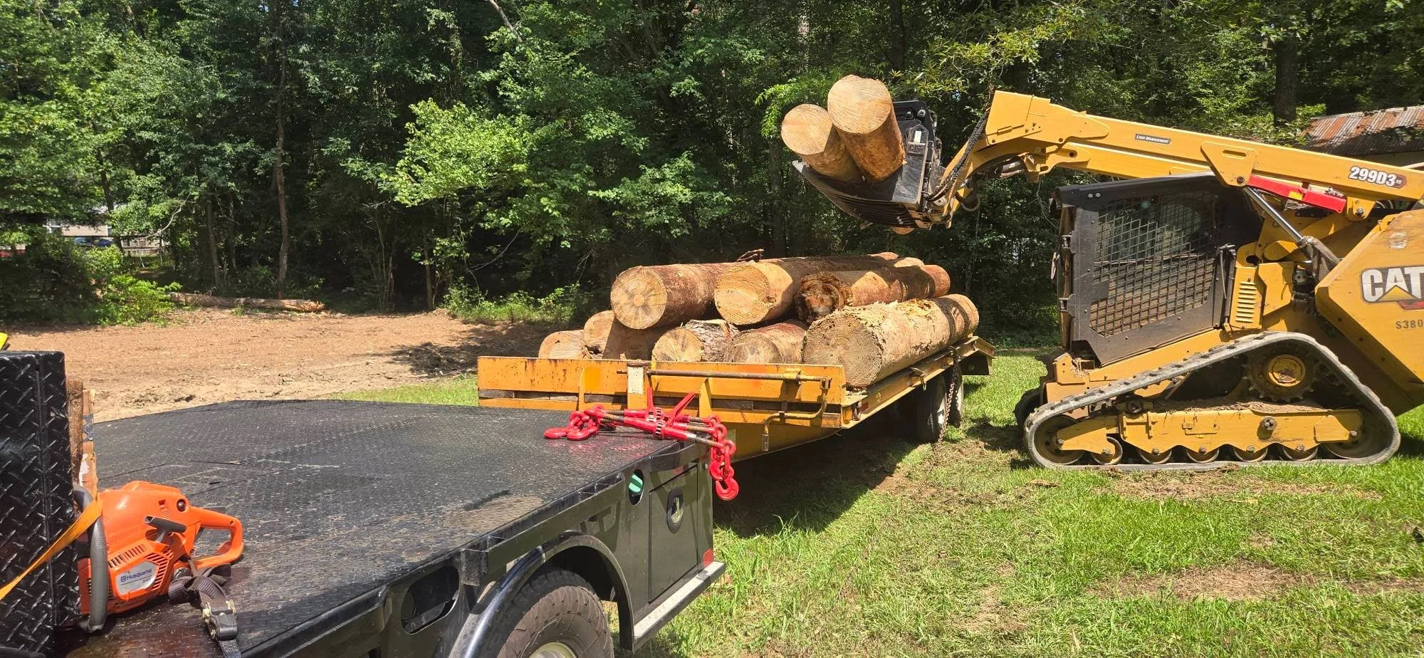 CAT skid steer with grapple loading cut logs onto trailer during land clearing operation