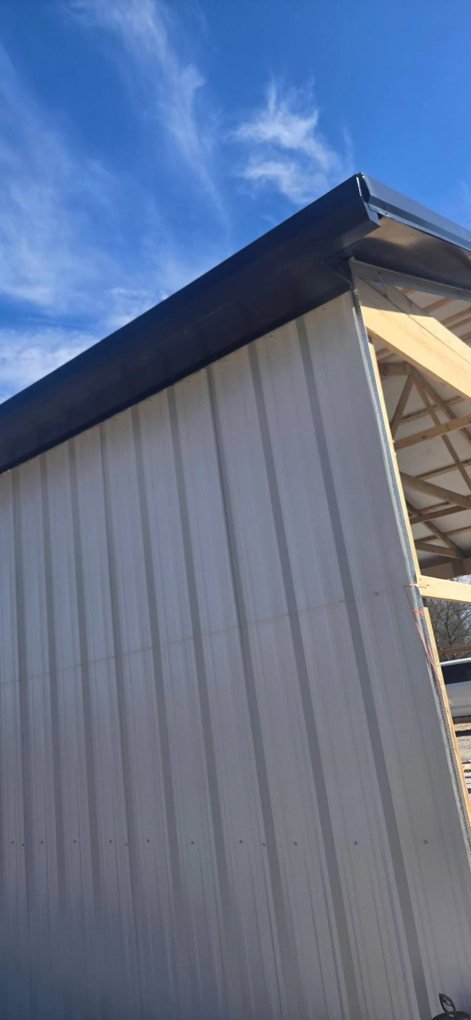 Metal carport with white corrugated siding, dark roof beam, and wooden truss framing